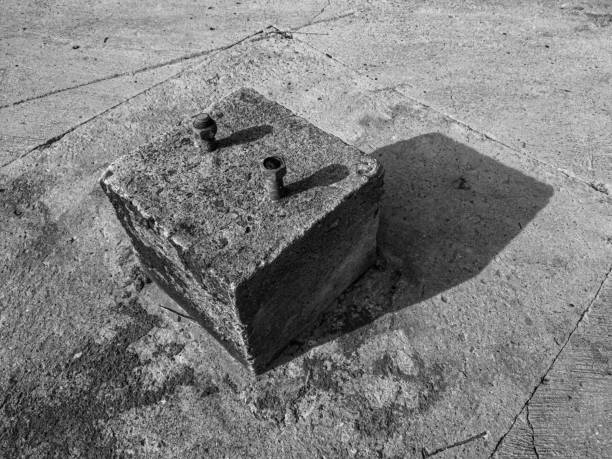 black and white abstract photography. a cubical shape made of concrete with two bolts on it