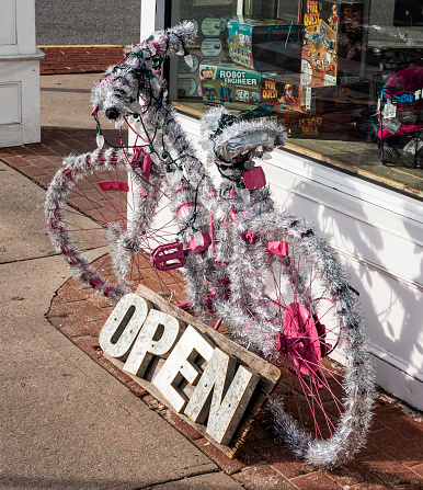 Babylon, New York, USA - 2 January 2019: A vibrant and enchanting sight awaits passersby as they encounter a gleaming bicycle adorned with shimmering tinsel, exuding the holiday spirit, outside a charming store.