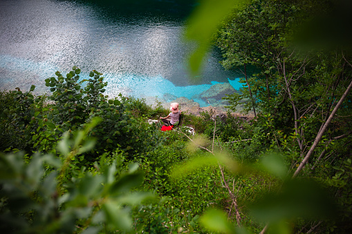 Young Adult Female Casual Cloths Tourist Meditation Exercises in natural beautiful Environment of an Turquoise Colored Mountain Lake