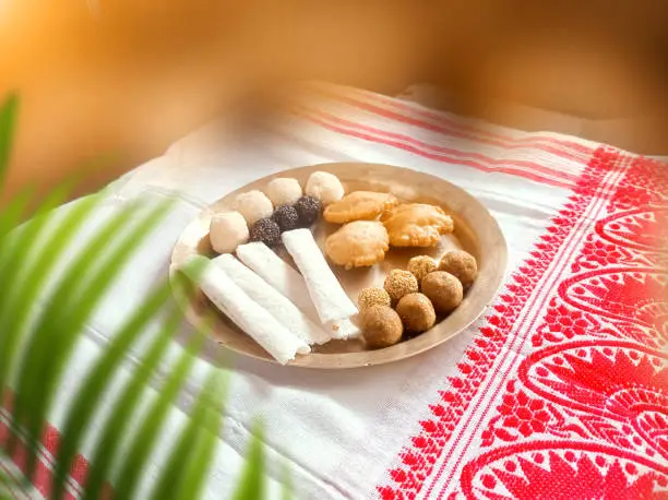 Assamese traditional food items like pitha, laddu, doi sira with assamese gamosa background with japi motifs