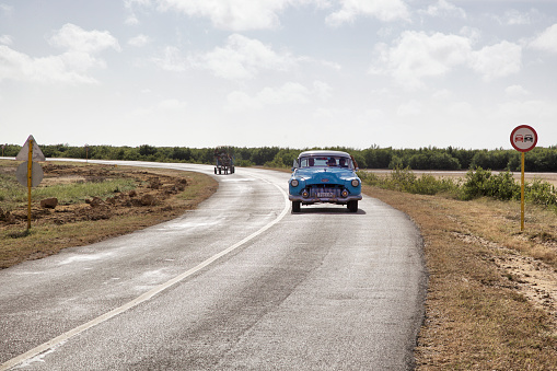 Trinidad, Cuba - January 4, 2015: Old American car and a horse drawn carriage on a rural road outside Trinidan, Sancti Spiritus, Cuba.