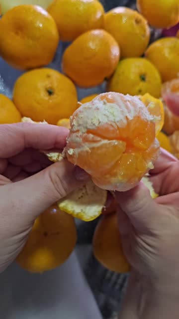 vertical peeling tangerines for the New Year, a woman in pajamas, close-up, hands peels a delicious juicy citrus fruit against the background of dark and yellow wallpaper holiday appetite vitamin C