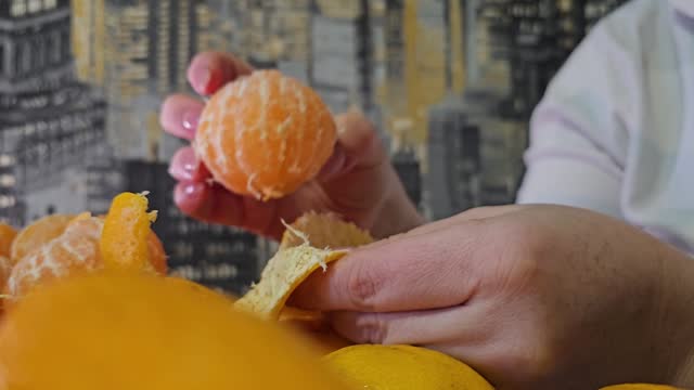 peeling tangerines for the New Year, a woman in pajamas, close-up, hands peels a delicious juicy citrus fruit against the background of dark and yellow wallpaper holiday appetite vitamin C