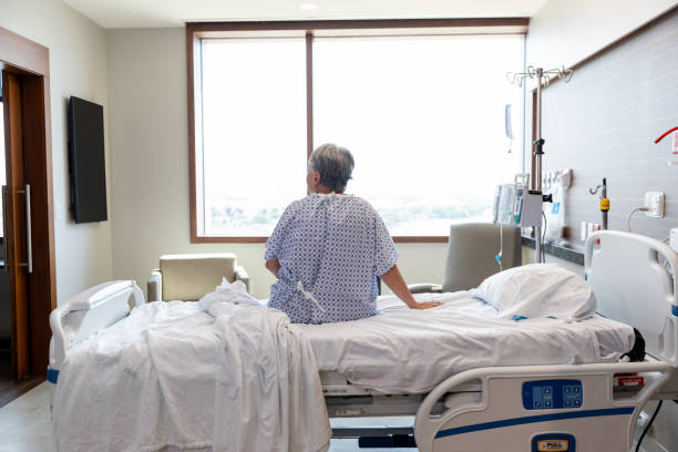 istock Alone in room, senior woman in gown sits on gurney 1945084607