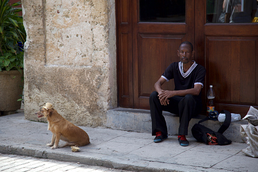 Havana, Cuba - January 1, 2015: Man with a cute dog on the sidewalk in Old Havana, Habana Vieja, Cuba.