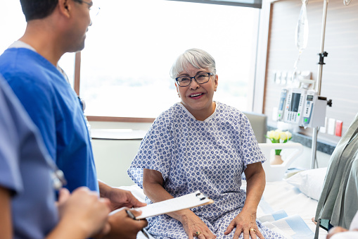 The mature female patient smiles while listening to her medical team give an update on her test results.