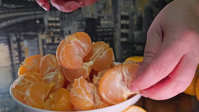Place peeled tangerines on a white plate and divide them into slices. Female hands prepare citrus fruits for tangerine juice.