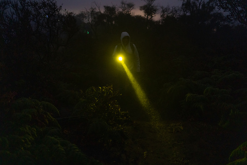 Front view of night man walking with flashlight. Tourist searching road in darknese jungle