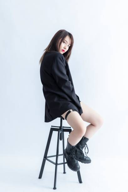 A young woman in a black suit is sitting on a stool.