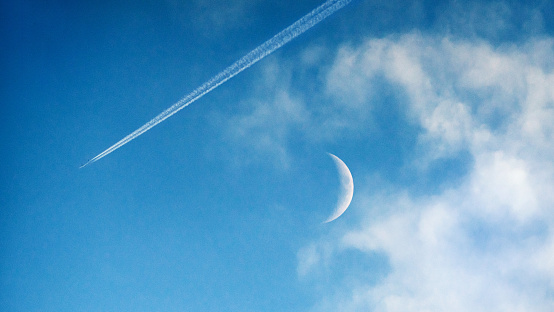 Daylight crescent moon and plane flying in the sky