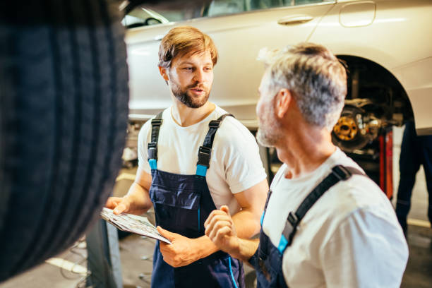istock Car service station. Two different age bearded attractive mechanics men standing and looking at each other checking engine errors to tune sport vehicle on lift. 1945208375