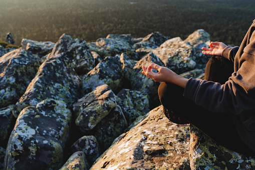 Close-up meditation in the mountains, yoga practice in the fresh air, women's hands on lap folded in chinmudra, omchanting, hatha yoga, calming the mind, health of body and soul
