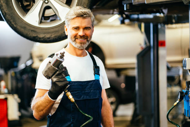 istock Bearded handsome grey haired male worker using impact wrench in garage. 1945230325