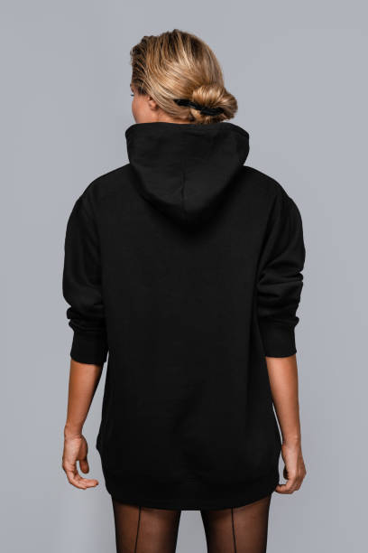 istock Woman dressed in a black oversized hoodie with blank space, ideal for a mockup, set against gray background 1945282911