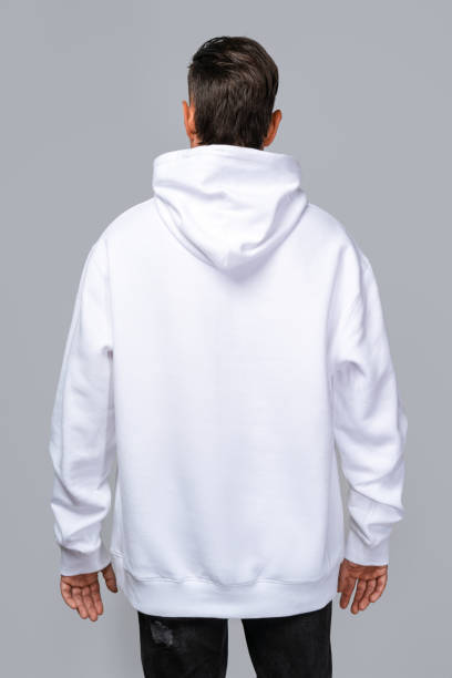 istock Man dressed in a white oversized hoodie with blank space, ideal for a mockup, set against gray background 1945291389
