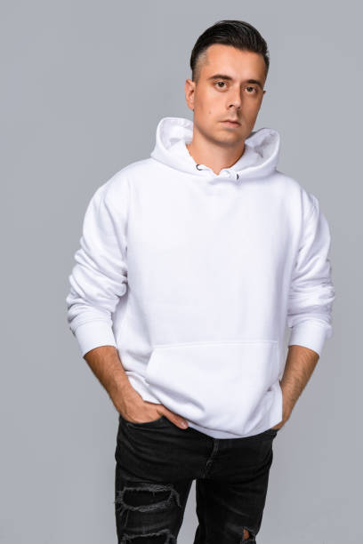 istock Man dressed in a white oversized hoodie with blank space, ideal for a mockup, set against gray background 1945291934