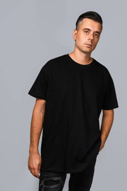 istock Man dressed in a black oversized t-shirt with blank space, ideal for a mockup, set against gray background 1945292463