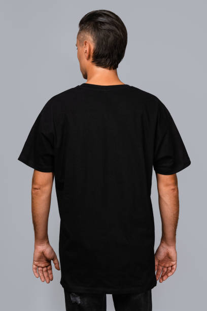 istock Man dressed in a black oversized t-shirt with blank space, ideal for a mockup, set against gray background 1945293484