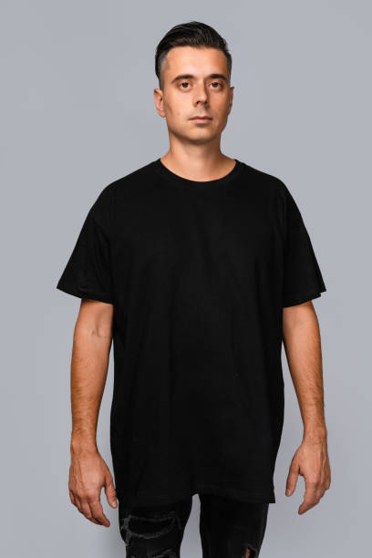 istock Man dressed in a black oversized t-shirt with blank space, ideal for a mockup, set against gray background 1945294001