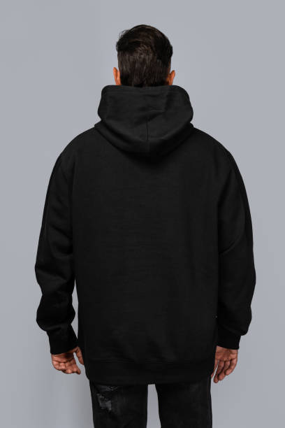 istock Man dressed in a black oversized hoodie with blank space, ideal for a mockup, set against gray background 1945294512