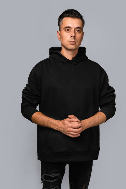 istock Man dressed in a black oversized hoodie with blank space, ideal for a mockup, set against gray background 1945295041
