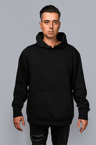 Man dressed in a black oversized hoodie with blank space, ideal for a mockup, set against gray background.