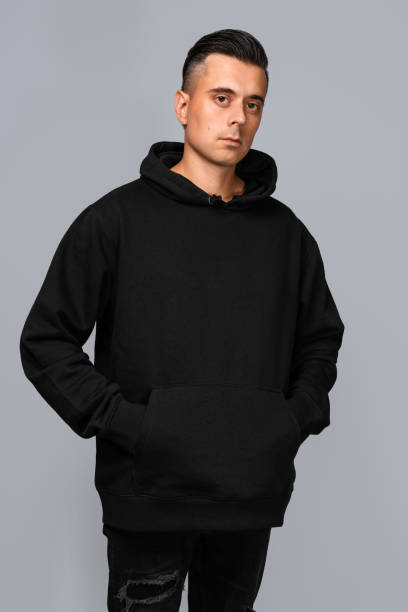 istock Man dressed in a black oversized hoodie with blank space, ideal for a mockup, set against gray background 1945296604