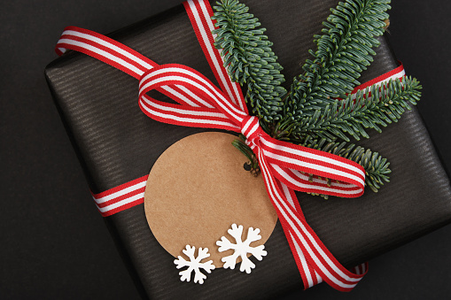 Fragment of gift box with fir tree sprig, snowflakes and label on dark background. Closeup. Space for your text