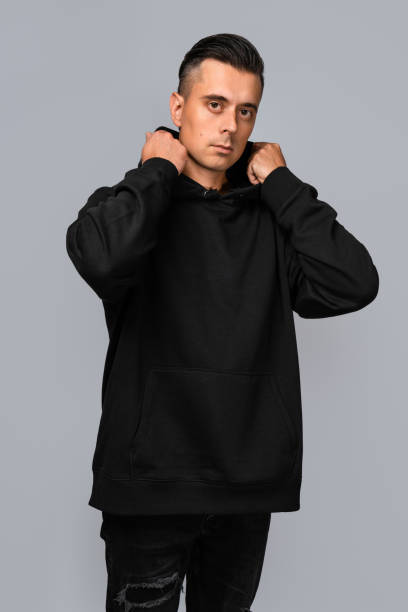 istock Man dressed in a black oversized hoodie with blank space, ideal for a mockup, set against gray background 1945297131