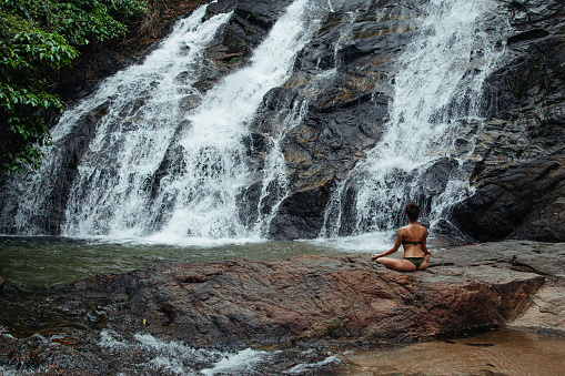 Young Woman in Swimsuit Practicing Yoga Near Waterfall in Rainforest.