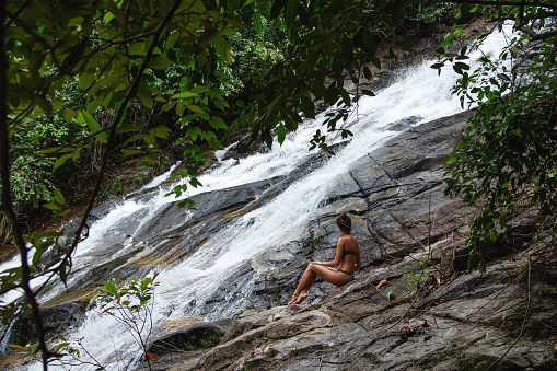 Beautiful Young Woman in Swimsuit Posing Near Waterfall.