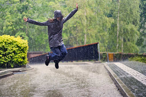 Teenage girl jumping in the rain with arms outstretched. The girl is enjoying the spring rain.\nShot with Canon R5