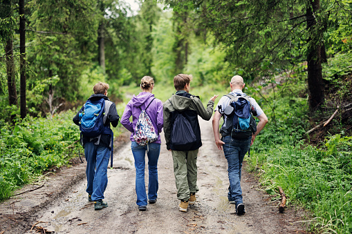 Father and three teenage kids hiking in Beskid Sądecki mountain range in Poprad Landscape Park, Poland.\nThey are walking on a dirt road leading deep into a lush, green forest.\nShot with Canon R5.