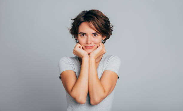 portrait en gros plan d’une jeune femme mignonne et tendre et magnifique aux cheveux courts bouclés en t-shirt gris. une fille regarde directement devant la caméra, isolée en studio. - straight hair women short hair human eye photos et images de collection