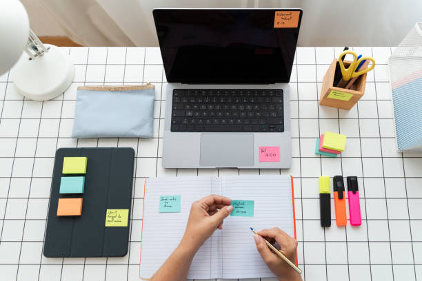 istock Person Writing on Paper Next to Laptop for Work or Study 1945364652