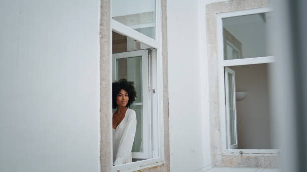 istock Tender model leaning window frame white house. Curly woman posing camera alone 1945389063