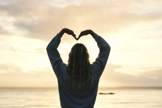 istock A woman forming heart shape at the beach at sunset 1945429228