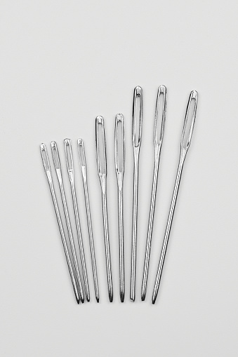 Set of silver sewing needles of different sizes isolated on white background top view, flat lay