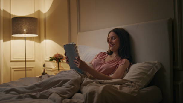 istock Peaceful woman reading book in evening home. Smiling reader enjoying novel rest 1945441330