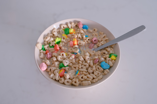 bowl with multicolored cereal with milk and spoon on white counter top, kids meal