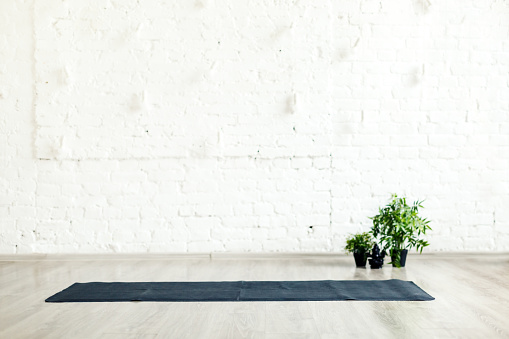 Unrolled yoga mat laid on the floor in empty space with white brick wall background, nobody. Concept of place for yoga, gymnastics, training, meditating