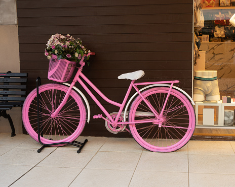 A pink women's bicycle with various colored roses in the front basket