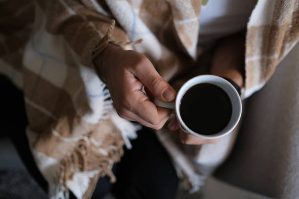 istock Man with blanket drinking coffee on cold winter morning 1945538395