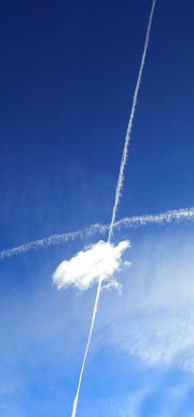 long white trails high in the blue sky crossing a cloud without airplanes