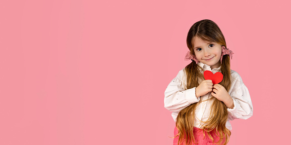 Excited little girl holding a red paper heart to her chest Valentine's day concept pastel pink bumblebee. High quality photo