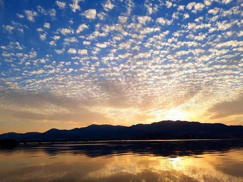 Clear sunset sky with scaly clouds and reflections on the mountains and lake