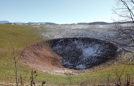 large depression in the terrain with snow in the mountains caused by the explosion of a mine in the First World War