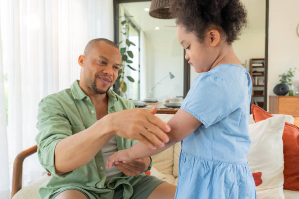 istock Happy black father sitting on a sofa and helping his elementary-aged child on dressing and taking a skin care at a cozy living room showing the bonding and responsibility of the father. 1945615783