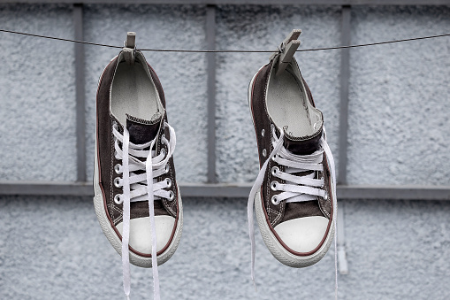 A pair of old black sneakers hanging on the clothesline with a clothespin, with a blurred background.