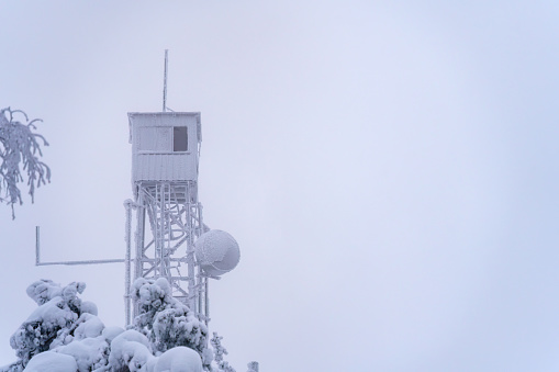 Frozen fire tower against white overcast sky in winter, copy space.